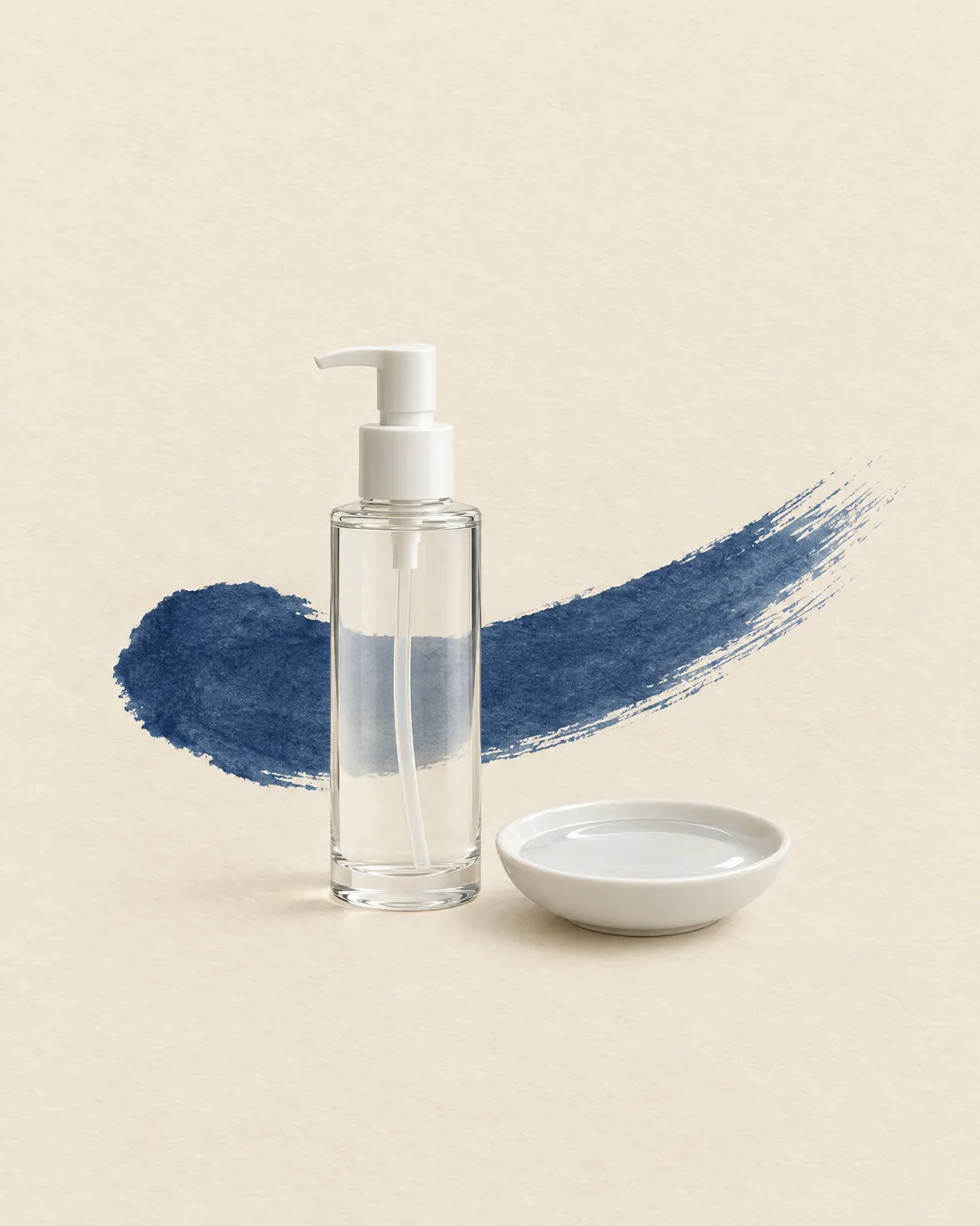 A clear glass bottle of nuru gel and a small porcelain dish, with a stroke of indigo ink behind